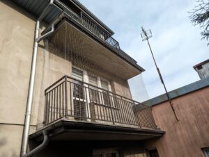 Siatka na balkon w domu jednorodzinnym na pierwszym piętrze w Mińsku Mazowieckim. Beżowa siatka zlewa się z szarą elewacją budynku.