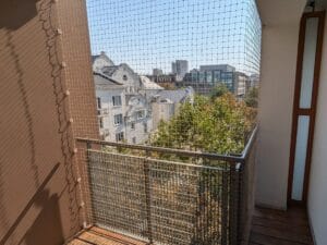 Siatka zamontowana na nietypowym balkonie. Balkon z wewnętrznym narożnikiem na warszawskiej Pradze. Estetyczny montaż na dość skomplikowanym balkonie z drewnianą podłogą.