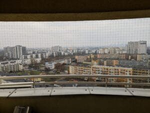 Siatka na balkon typu loggia na 13 piętrze wieżowca. Siatka zmontowana dla niesfornego kociaka. W tle panorama Warszawy.