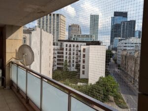 Siatka zainstalowana na balkonie w centrum Warszawy. W tle wieżowce z centrum Warszawy. Siatka z możliwością otwierania w celu serwisowania anteny satelitarnej.