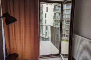 Widok z wewnątrz mieszkania na balkon na którym zamontowana jest siatka dla kota.
